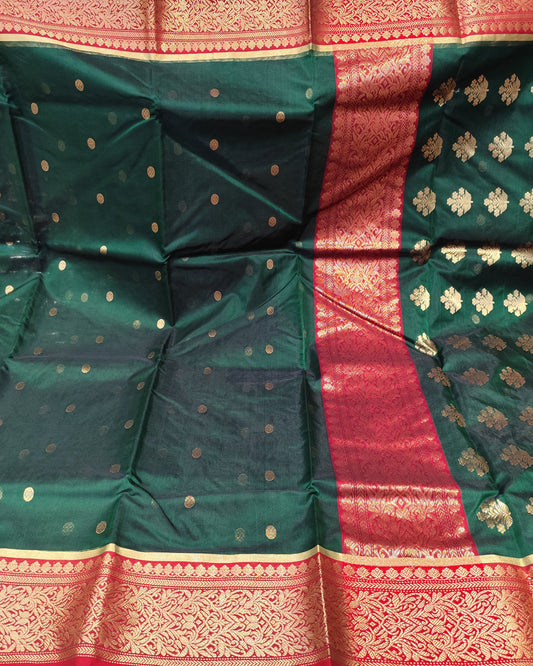 A close-up of a dark green silk saree fabric with gold zari motifs, a red border, and gold floral patterns.