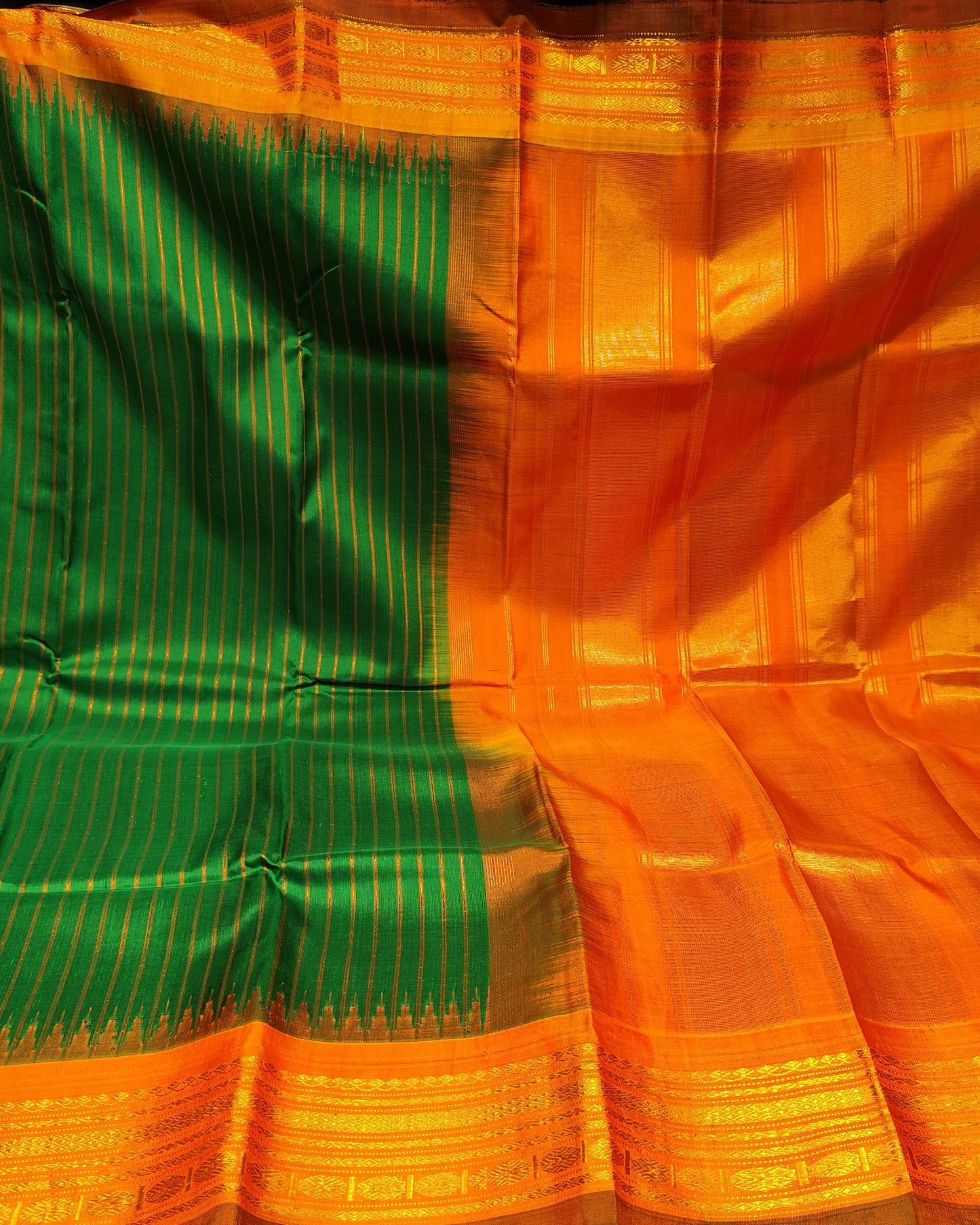 An orange and green silk saree with gold zari stripes and a wide gold border, draped to display its pattern and texture.