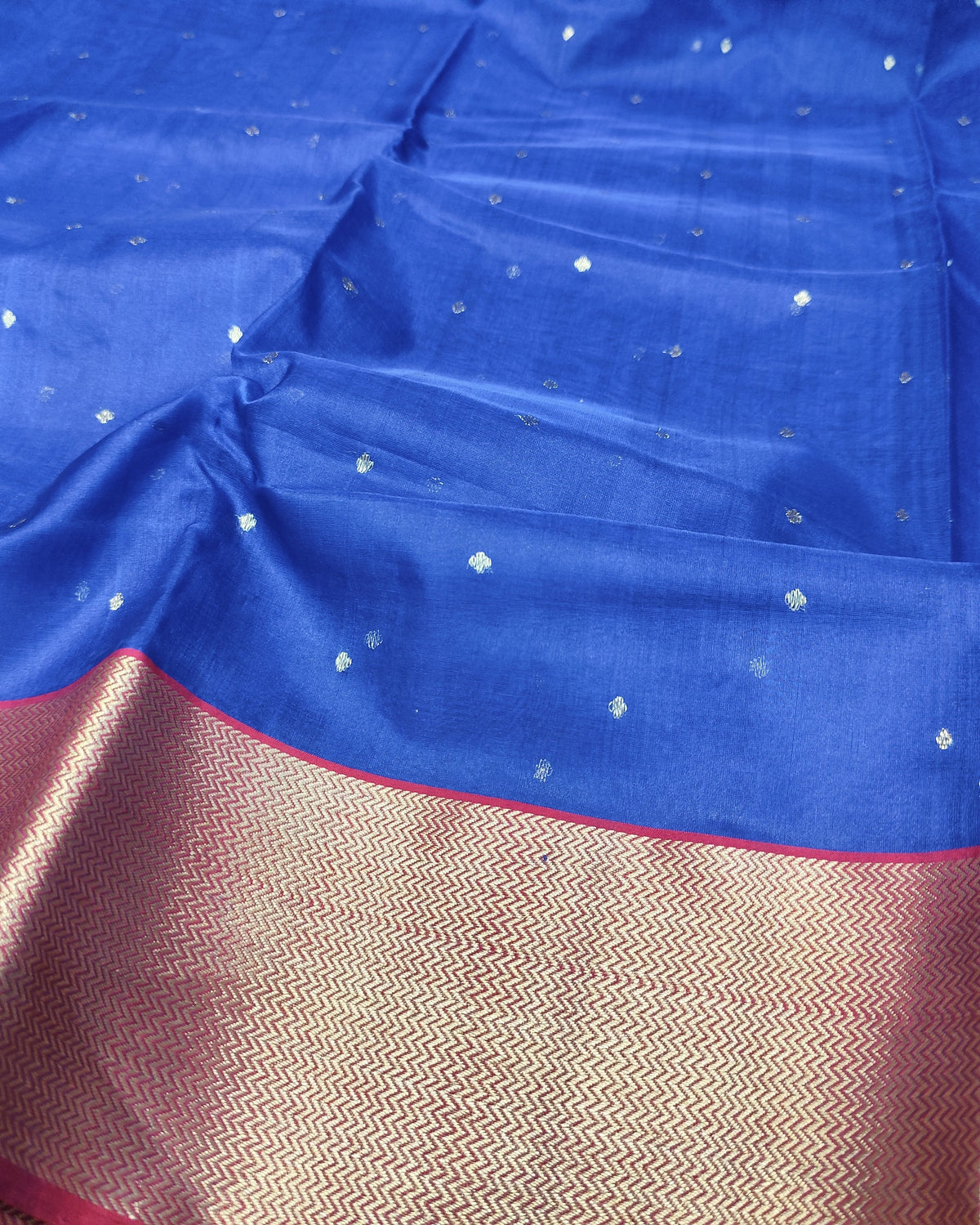 A royal blue silk saree with small metallic gold motifs and a wide gold zari border with pinkish-red edges.