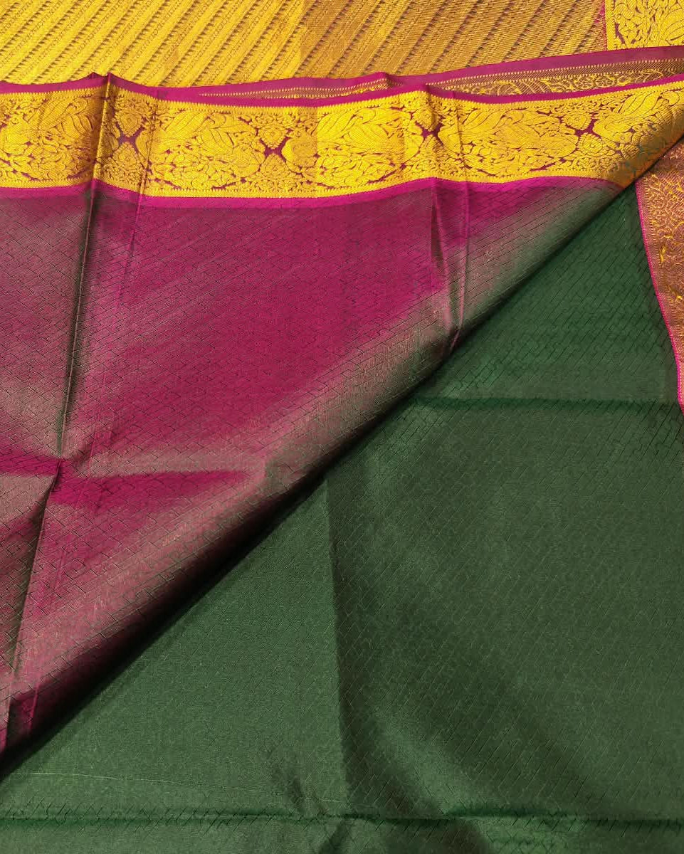 A close-up of a folded silk saree showing a dark green body, a magenta pink border, and a golden-yellow zari-painted pallu.
