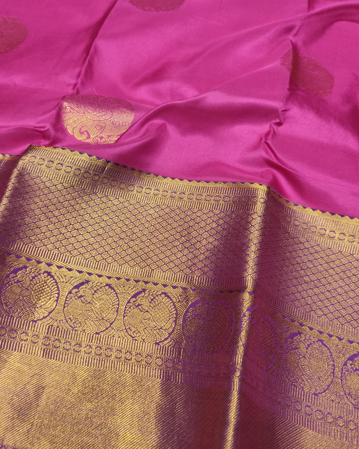 A close-up of a Kanjeevaram Silk Orange & pink silk saree with a wide gold zari border featuring intricate woven motifs.