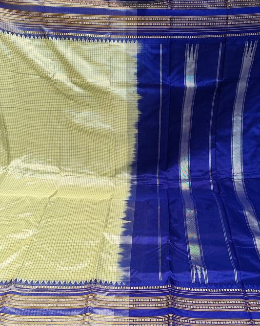 A blue and beige silk saree with intricate metallic zari patterns, displayed flat in a fabric store.