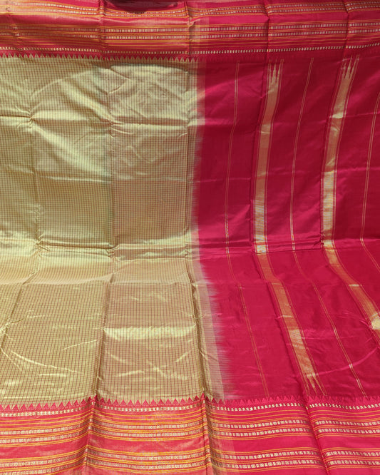 A folded and draped silk saree with a golden-beige body, a bright red border, and intricate gold zari stripes, displayed against a dark background.
