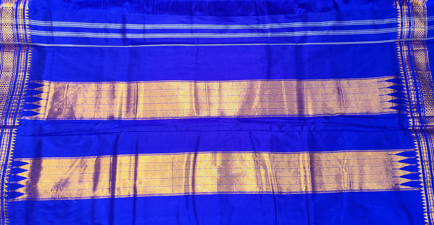 A pink and royal blue Ilkal silk saree from karnataka with gold zari stripes and a vibrant pink border, held up by a person in a shop setting.