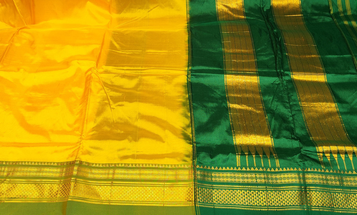 A yellow and green silk saree with gold zari borders, displayed flat on a table with stacks of folded fabrics in the background.