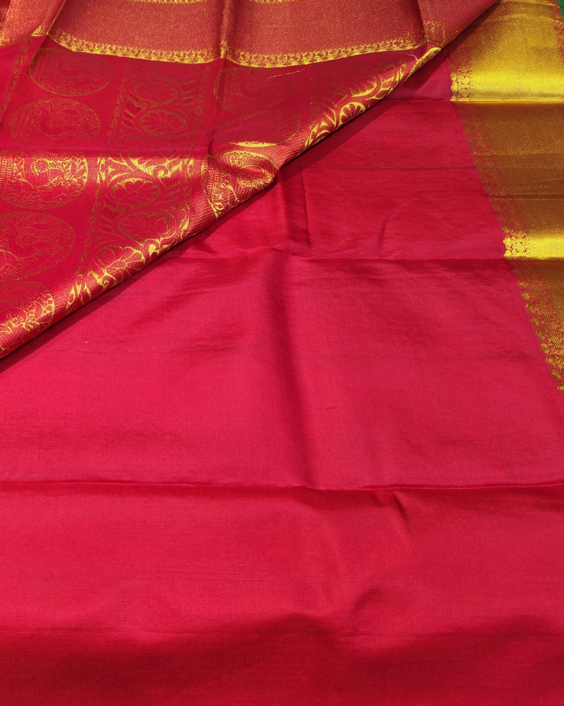 A bright red silk saree with a wide golden-yellow zari border and a matching red pallu, being held open to display its pattern and sheen.