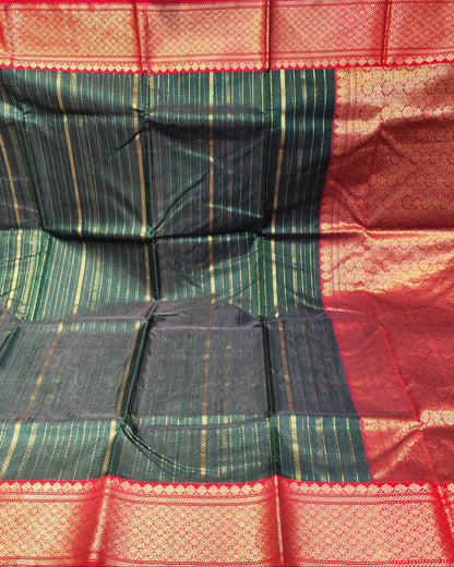 A dark green and red woven Chanderi sari with gold zari stripes and borders, held up by hands in a fabric store.