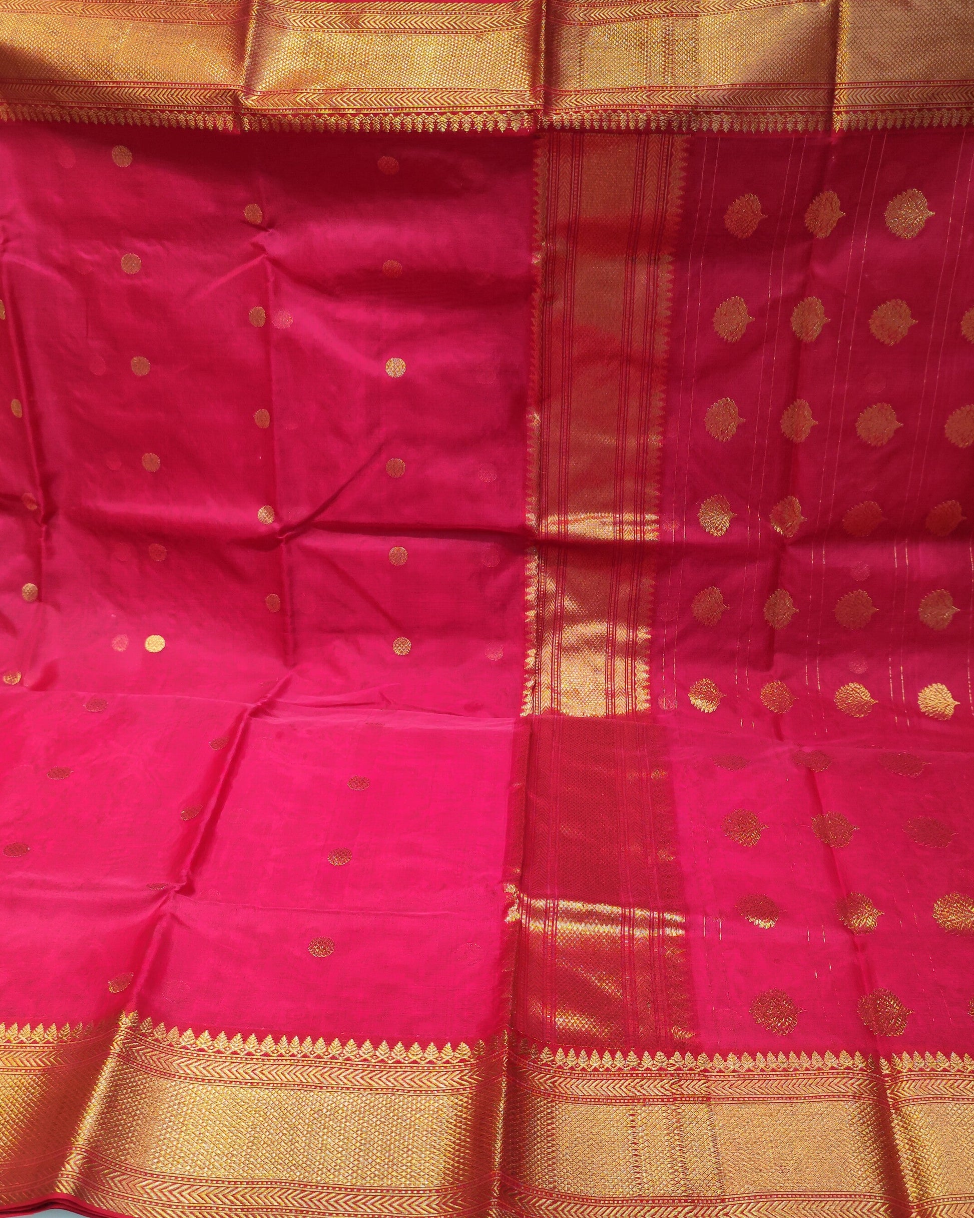 A bright red chanderi silk saree with gold zari motifs and borders, held up to display its full pattern and pallu in a fabric store.