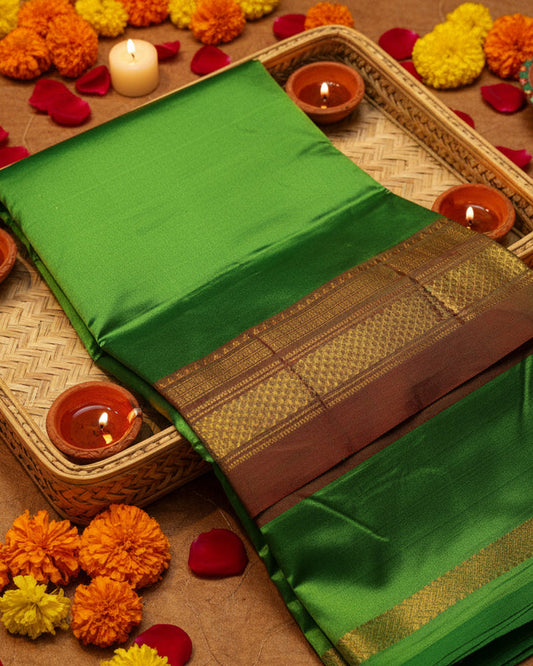 A folded green Ilkal silk saree with a wide golden zari border and a red inner layer, displayed on a plain off-white background.