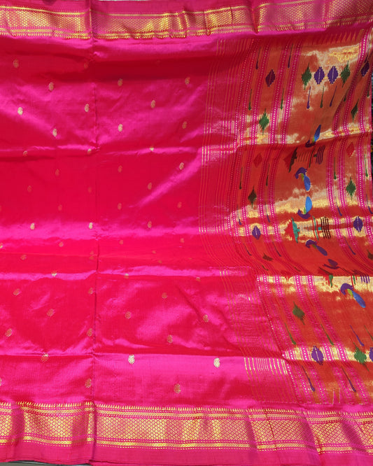A bright pink silk saree with gold zari woven borders and small gold motifs, displayed flat with the pallu section draped on the right side.