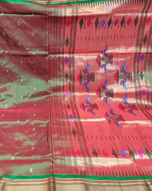 A folded and draped red and green silk saree with gold zari borders and multicolored ikat motifs, displayed against a background of folded other fabrics.
