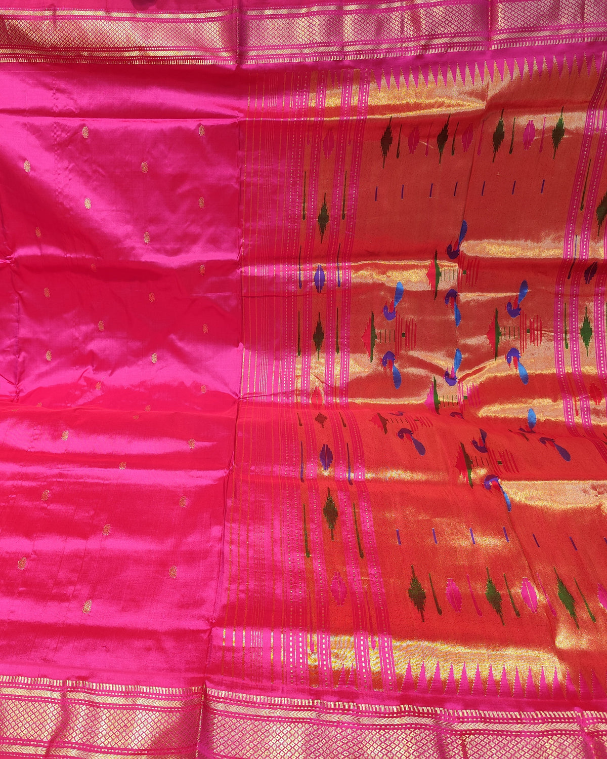 A bright pink silk saree with gold zari borders and small gold motifs, displayed flat with its pallu section showing geometric patterns.