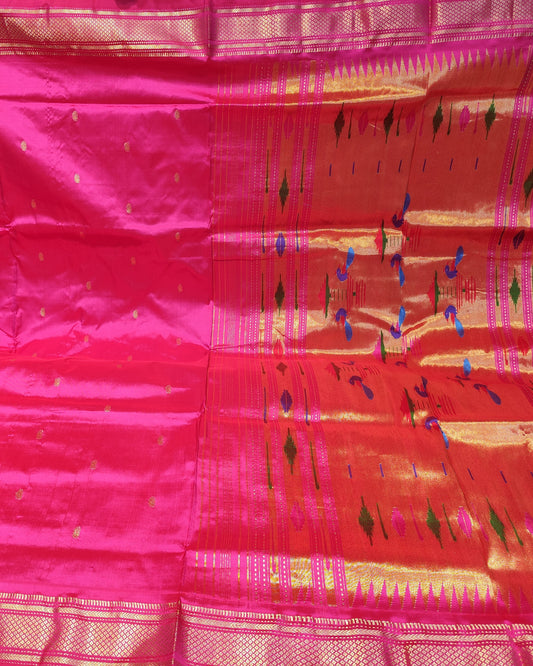 A bright pink silk saree with gold zari borders and small gold motifs, displayed flat with its pallu section showing geometric patterns.
