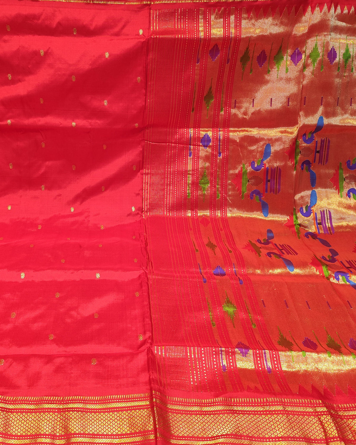 A bright red silk saree with gold zari borders and small gold motifs, displayed flat. The pallu (border) section features colorful embroidered floral patterns in blue, green, and purple.