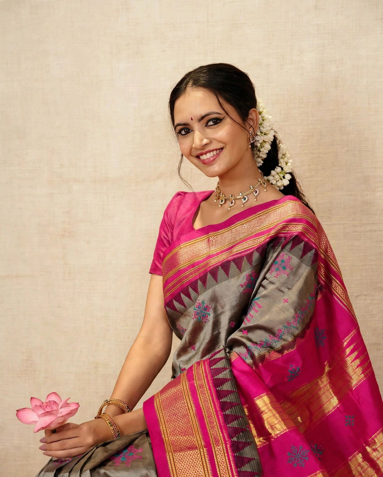 A woman wearing a traditional Indian silk Ilkal saree with a pink blouse, gray body, and vibrant magenta border with gold zari detailing. 