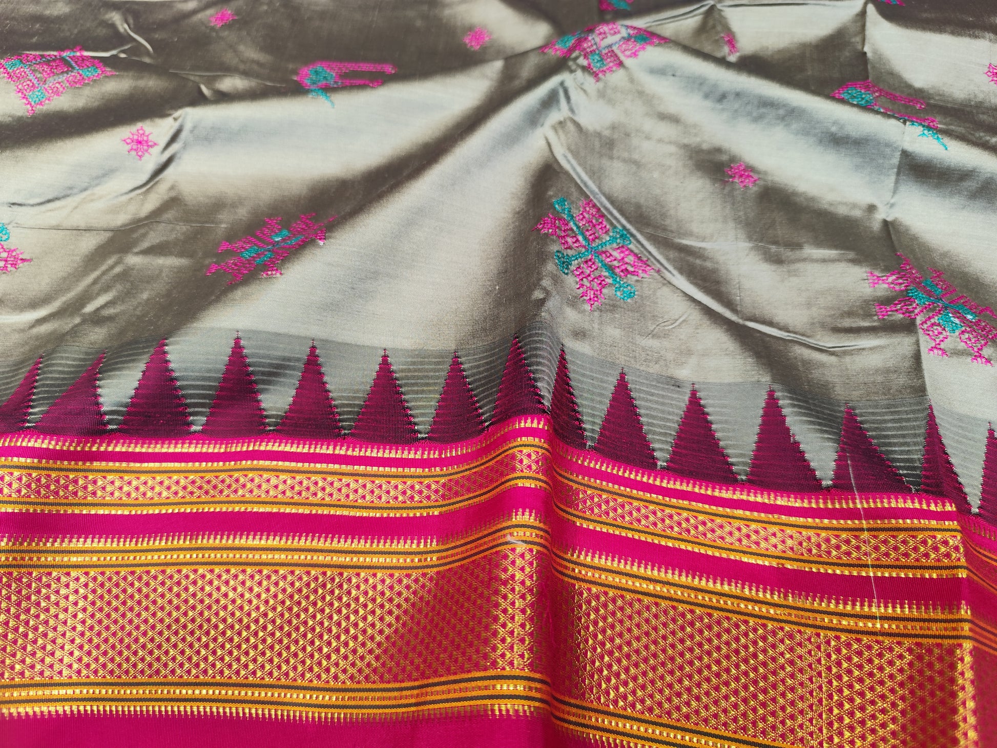 Ilkal grey slk saree with blue and pink kasuti inspired motifs and pink border. It has gold zari work.