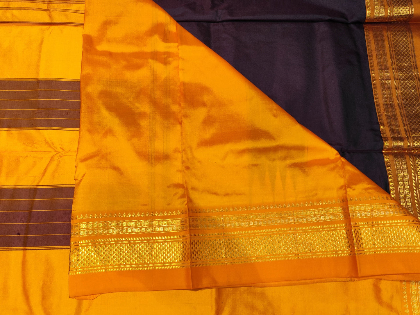 A close-up of a orange and brown silk saree with gold zari borders and a dark brown body, laid flat on a wooden floor.