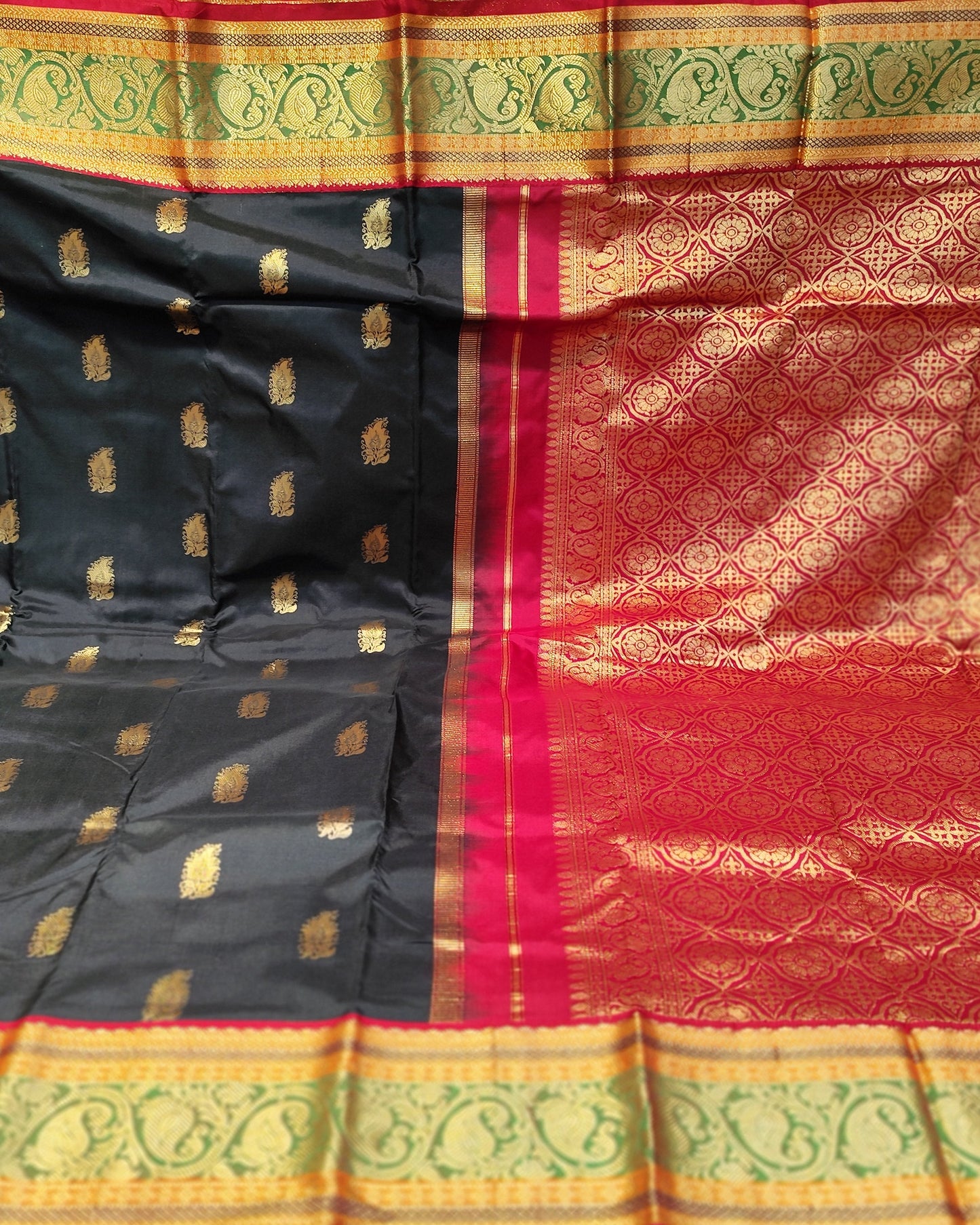 A black and red silk saree with gold zari brocade work, held up to display its pattern and borders in a fabric store.