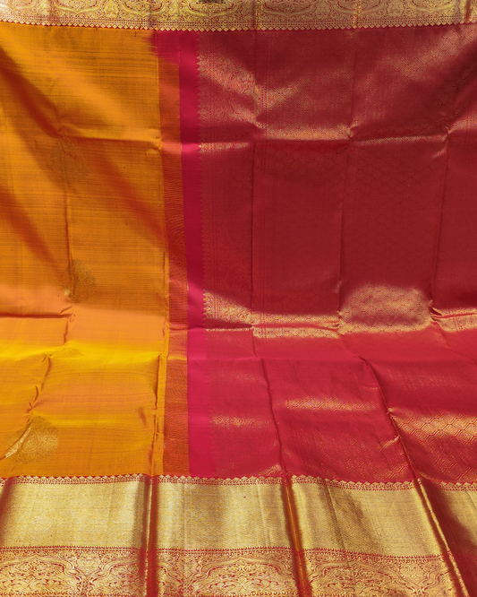A close-up of a richly colored silk saree, featuring a deep red body with a vibrant magenta border, a golden-yellow border, and ornate gold zari metallic weaving throughout.