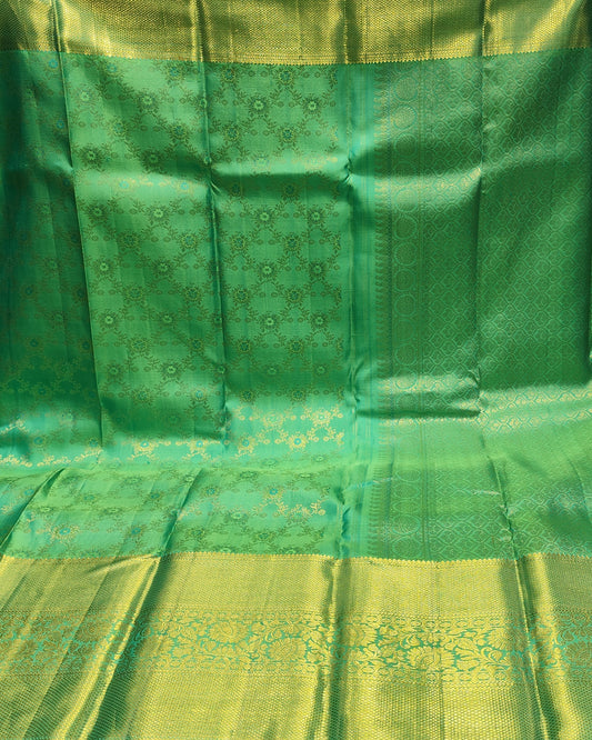 A green and gold silk saree with intricate woven patterns, draped to display its body, border, and pallu in what appears to be a shop setting.