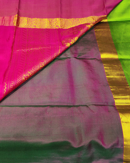 A folded and draped Kanjeevaram silk saree with a vibrant magenta-pink body, a dark green border, a bright lime green pallu, and ornate gold zari brocade patterns.