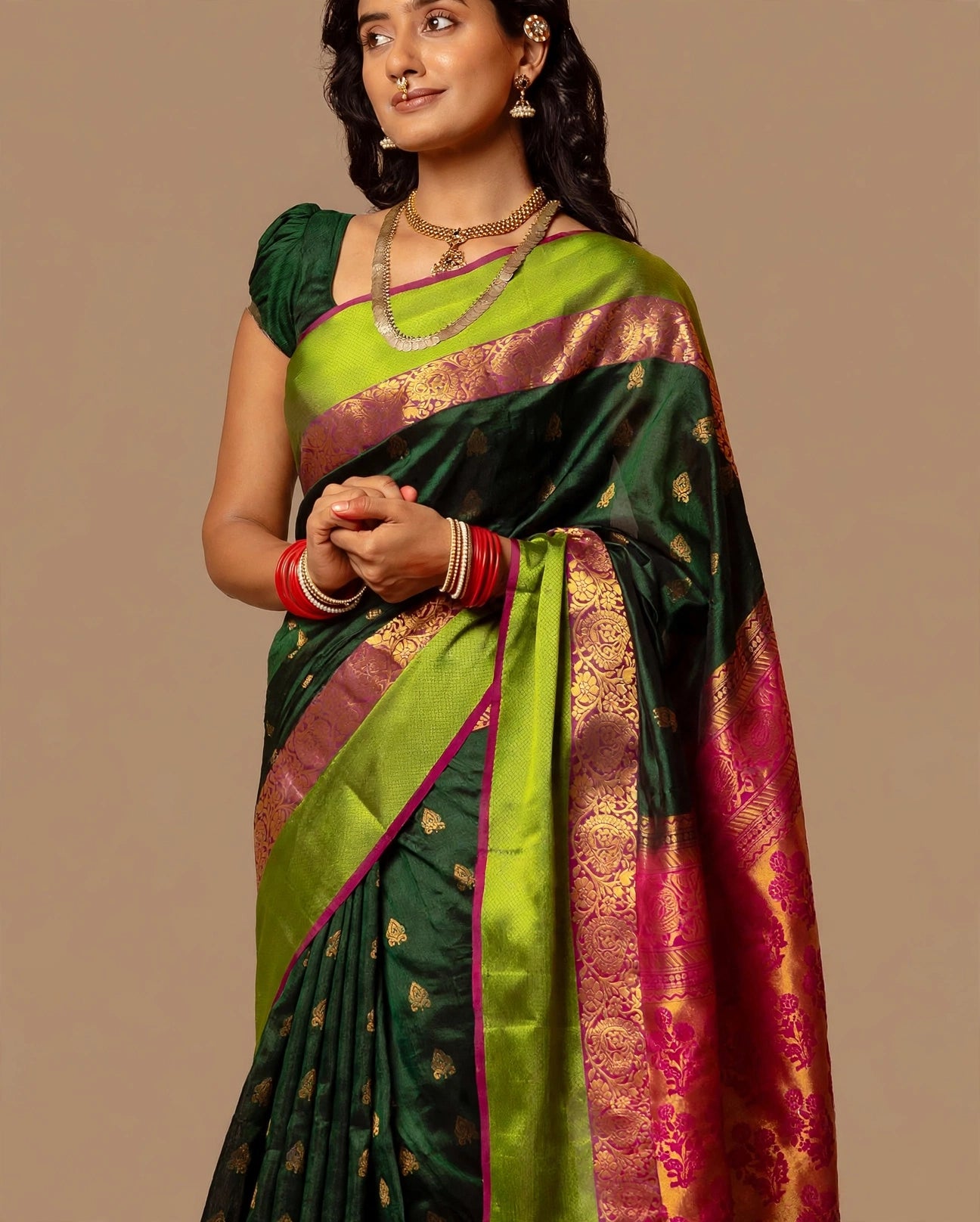 A woman modeling a Kanjeevaram Green & Pink saree with a bright lime green border, pink and gold zari woven patterns, and a matching pink border, set against a solid beige background.