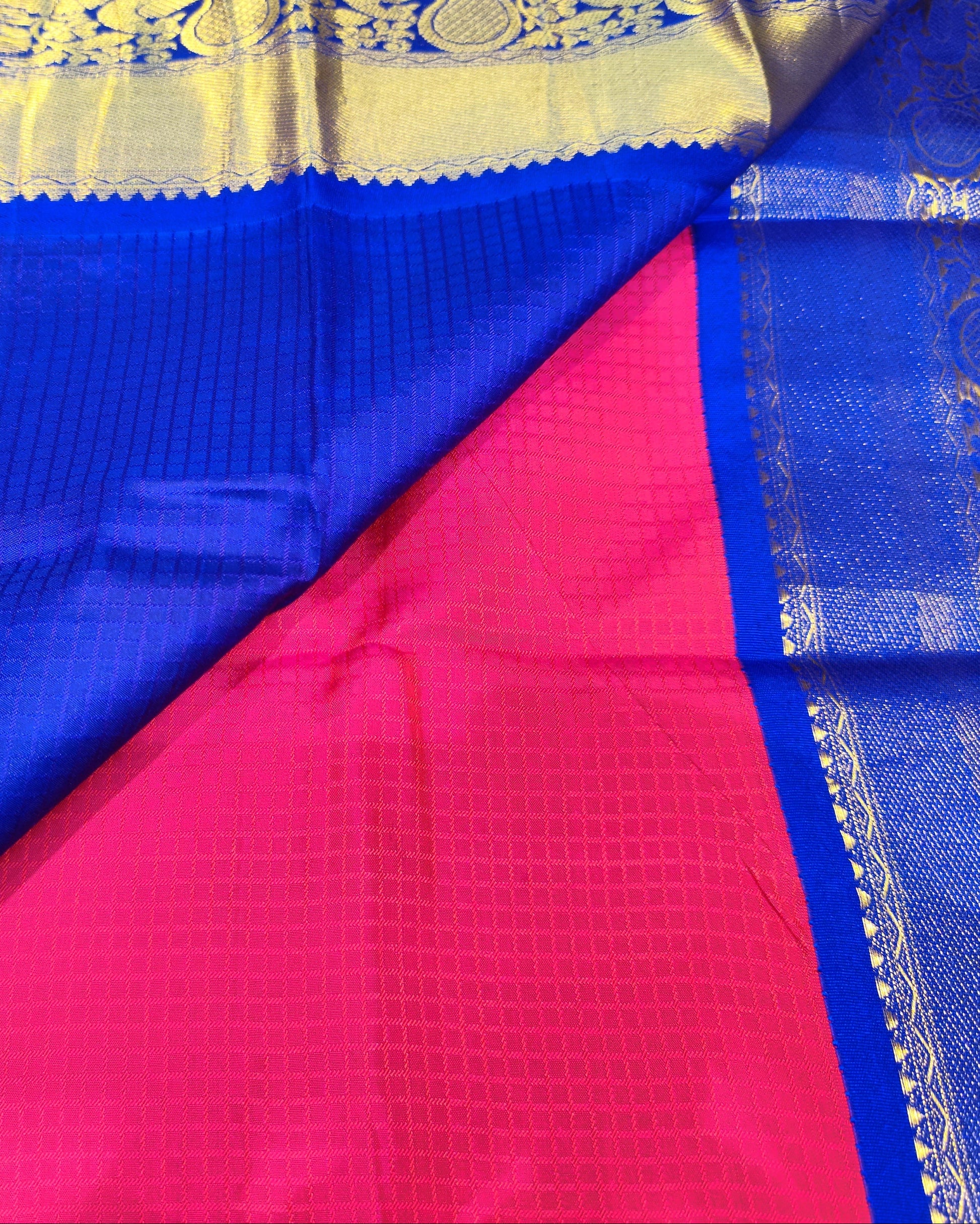 A royal blue and pink silk saree with intricate gold zari woven borders and motifs, displayed in a draped layout.
