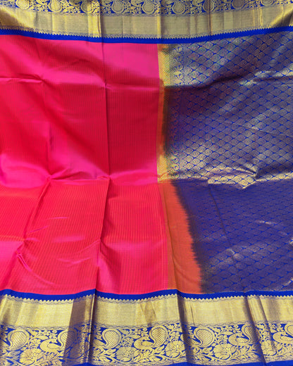 A vibrant pink and purple silk saree with intricate gold zari woven borders, displayed in a fabric store setting.