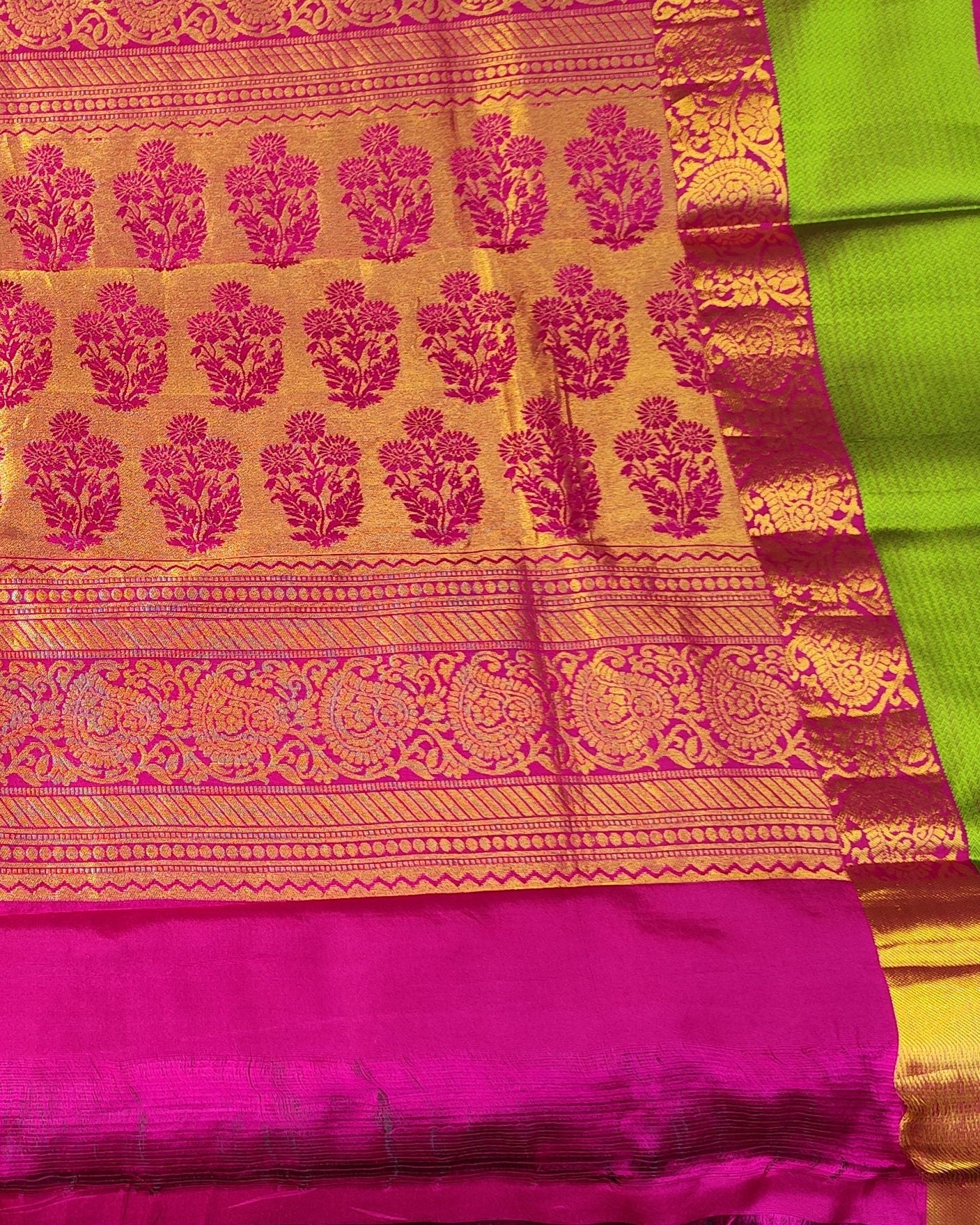 unfolded pink and gold brocade Kanjeevaram sari with a lime green border, showing off its intricate patterns and sheen in what appears to be a fabric store.