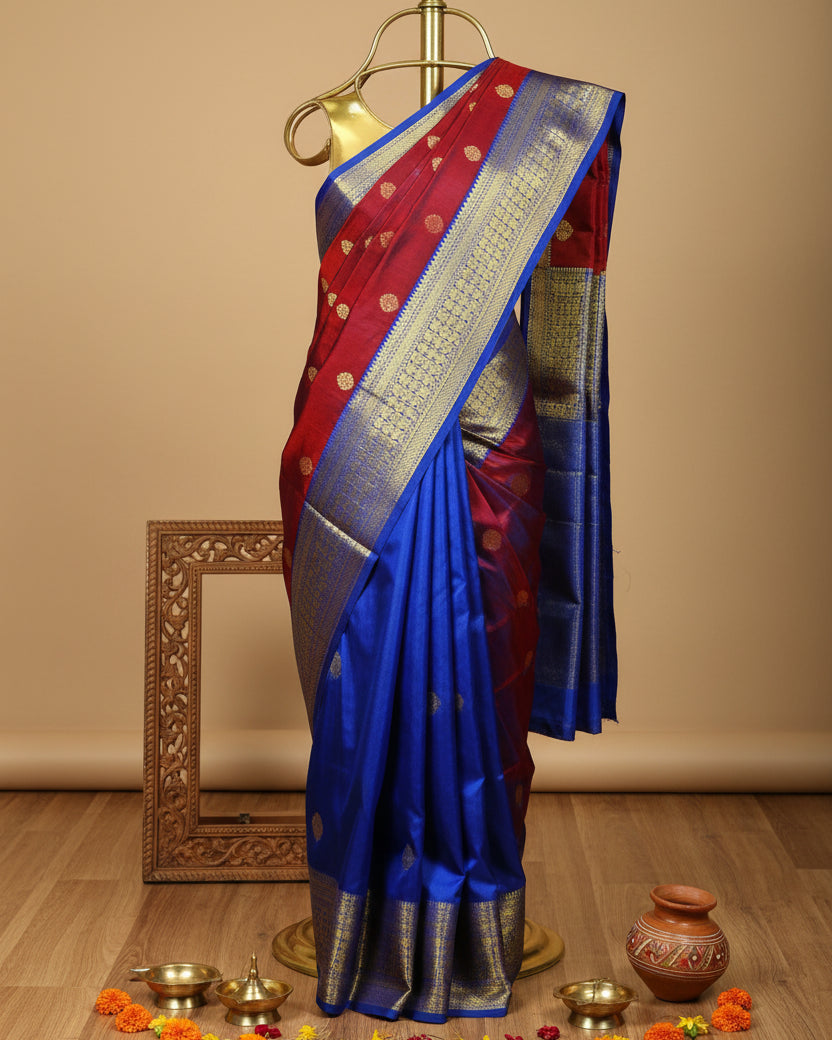 A folded and draped silk saree with a vibrant red body, a rich royal blue border, and detailed gold zari metallic patterns.