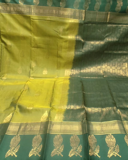 A green and yellow-green silk saree with intricate gold zari brocade patterns, displayed in a fabric store setting.
