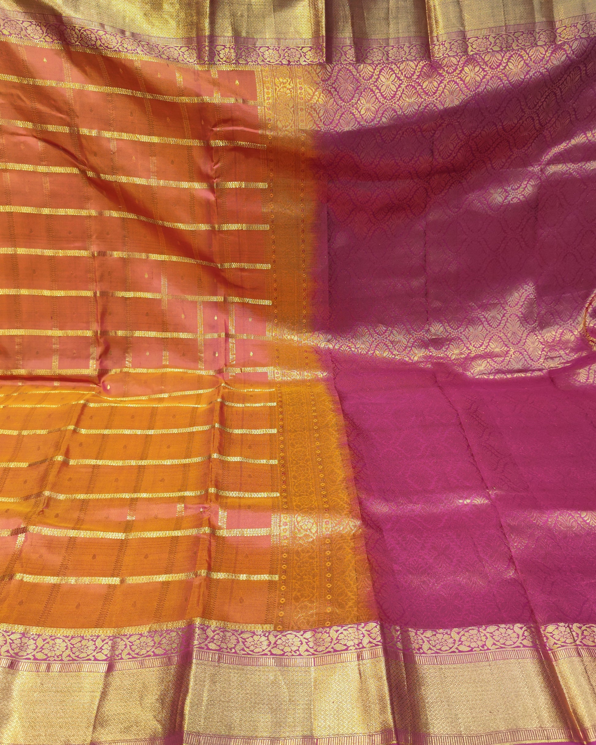 A folded and draped silk saree with a vibrant magenta-pink body, golden zari woven patterns, and a contrasting orange-yellow border with horizontal metallic stripes.