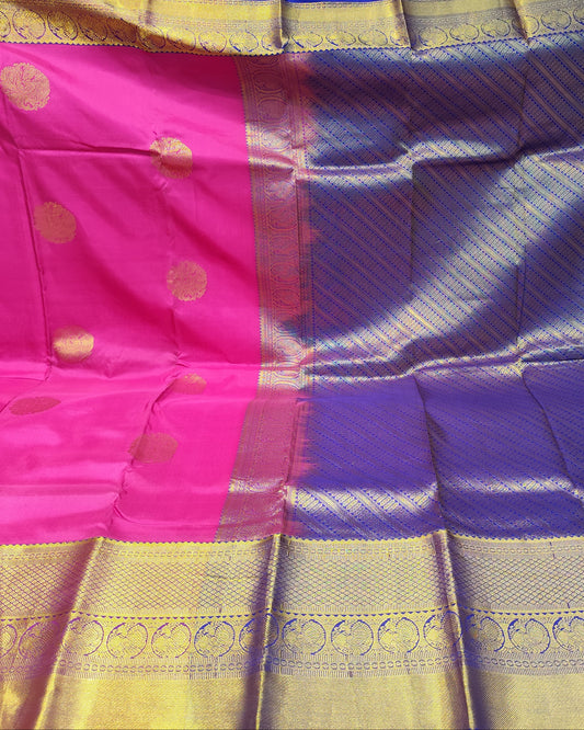 A folded and draped silk saree with a vibrant magenta pink body, a deep purple border, and a wide gold zari brocade border with metallic gold motifs.