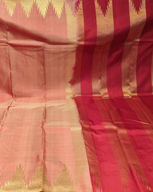 A peach and red silk saree with gold zari woven patterns, draped to show its body, border, and pallu in a fabric store setting.