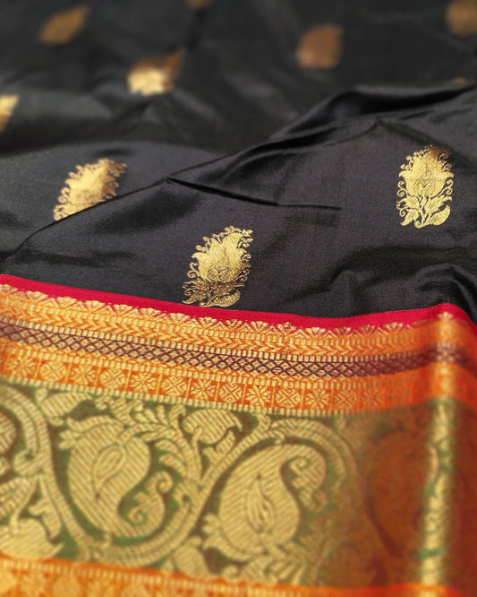 A close-up of a black silk saree with gold zari motifs and a wide orange and gold brocade border with red piping.