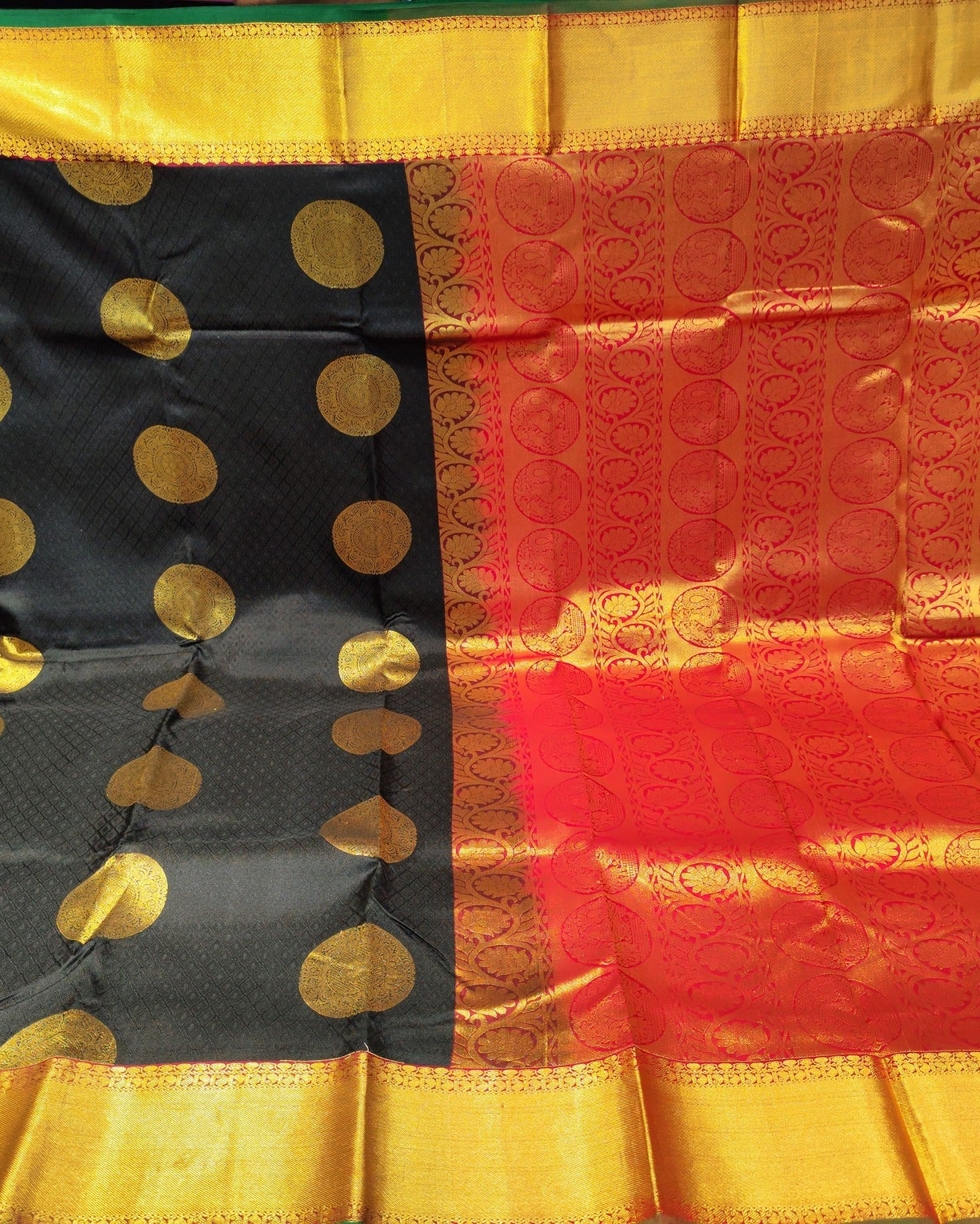 A black and red Kanjeevaramsilk saree with gold zari brocade work, held up by hands in a retail shop setting.