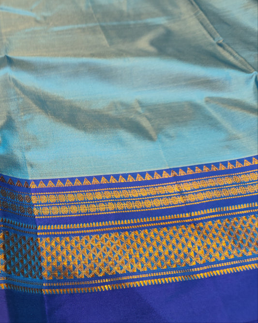 A close-up of a light blue silk Ilkal saree, featuring a wide decorative border with gold and purple woven patterns.