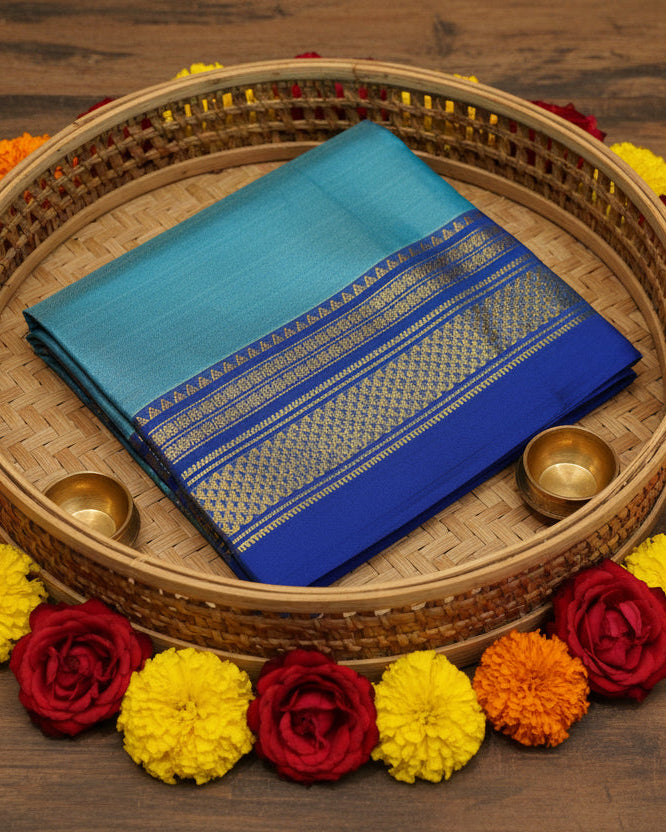 A folded blue Ilkal silk saree or sari, featuring a wide border with intricate gold and yellow woven geometric patterns, displayed against a plain off-white background.