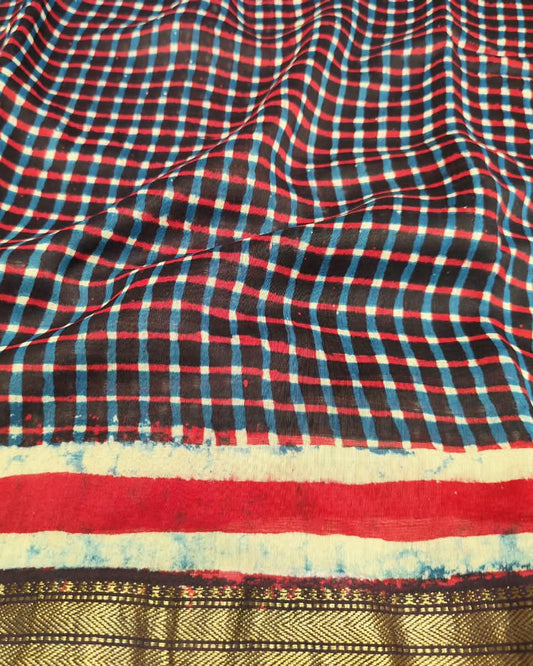 A close-up of a checkered Maheshwari Silk Cotton Saree | Black  with red, black, and light blue gingham, featuring a wide red stripe and a gold patterned border at the bottom.