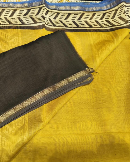 A folded black cotton fabric piece, likely a blouse piece or dupatta, laid flat on top of a yellow and blue patterned textile.