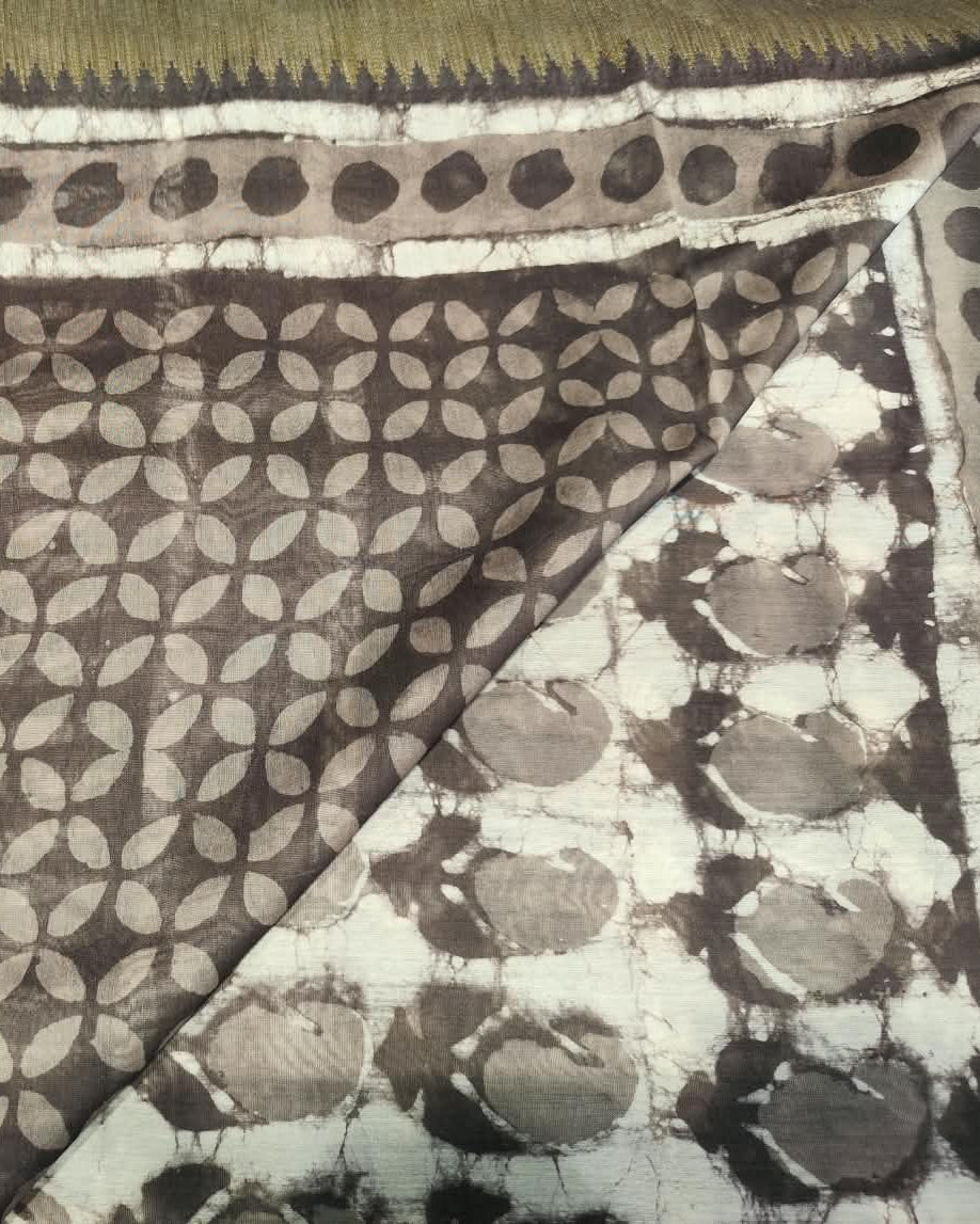 A close-up of a patterned Maheshwari Silk Gray 1 featuring a dark brown base with beige leaf-like block prints and a white border with black tie-dye style circular motifs.
