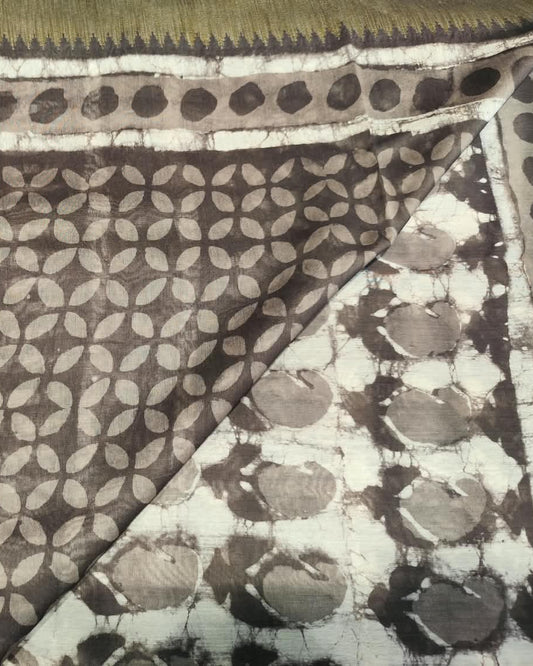 A close-up of a patterned Maheshwari Silk Gray 1 featuring a dark brown base with beige leaf-like block prints and a white border with black tie-dye style circular motifs.