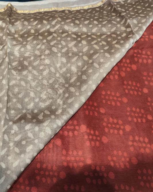 A close-up of a patterned tMaheshwari Silk Grey & Red Saree showing a taupe-beige section with white irregular spots and a rust-red section with red dots.