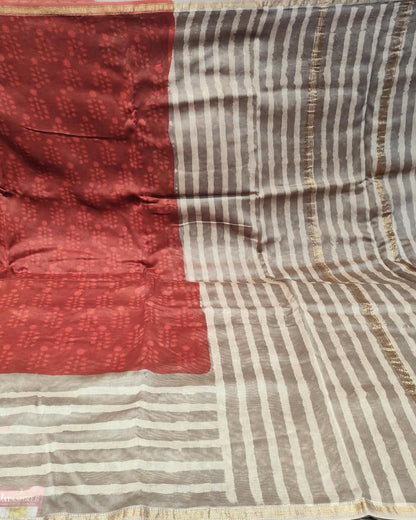 A close-up of a striped Maheshwari Silk Grey & Red  likely a saree, featuring a solid rust-red block on the left and vertical stripes of brown, beige, and gold on the right.
