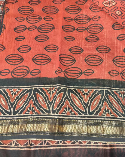 A close-up of a patterned Maheshwari Silk Red 1 featuring a coral red field with black geometric and floral motifs, a wide black border, and a decorative gold and black zari band.