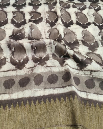 A close-up of a patterned fMaheshwari Silk Saree Gray 3 featuring a white base with dark brown tie-dye style paisley motifs and a wide border with a gold zari-like pattern.