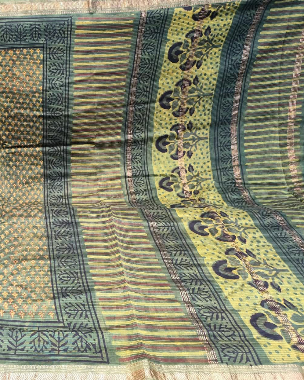A close-up of a patterned Maheshwari Silk Saree Green2 featuring a beige body with a green and gold geometric lattice pattern, a dark green border, and a yellow-gold pallu with floral motifs.