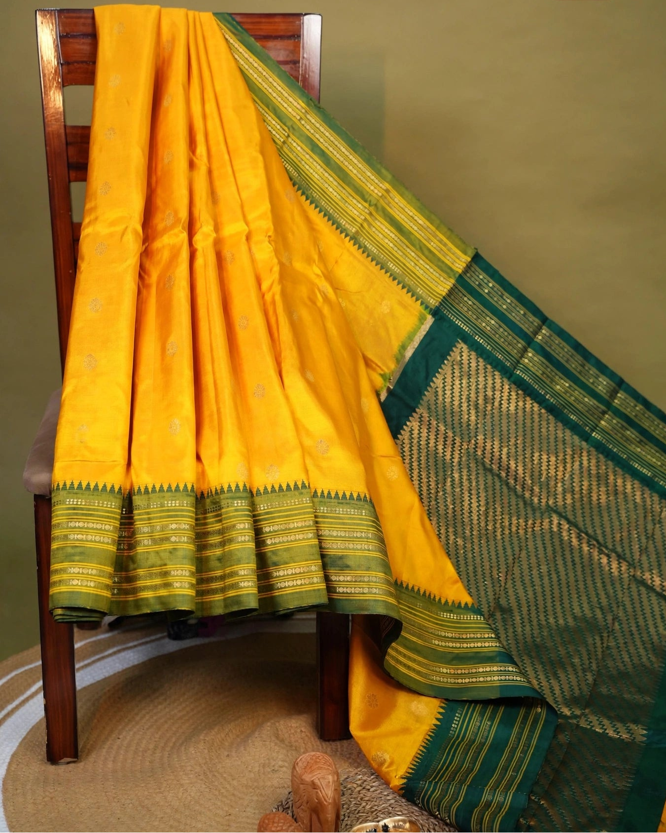 A Naranyanpeth yellow silk saree draped over a wooden chair against a solid olive green wall