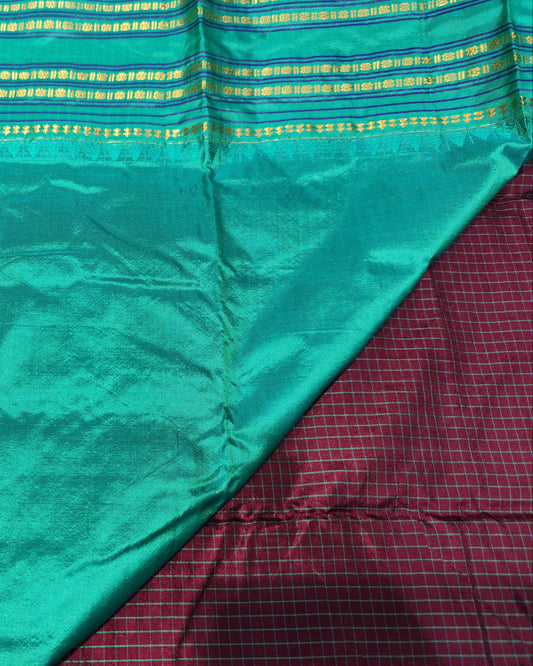 A close-up of a teal greensari, showing its sheen and texture. The fabric features horizontal rows of gold and yellow woven metallic patterns along the border.