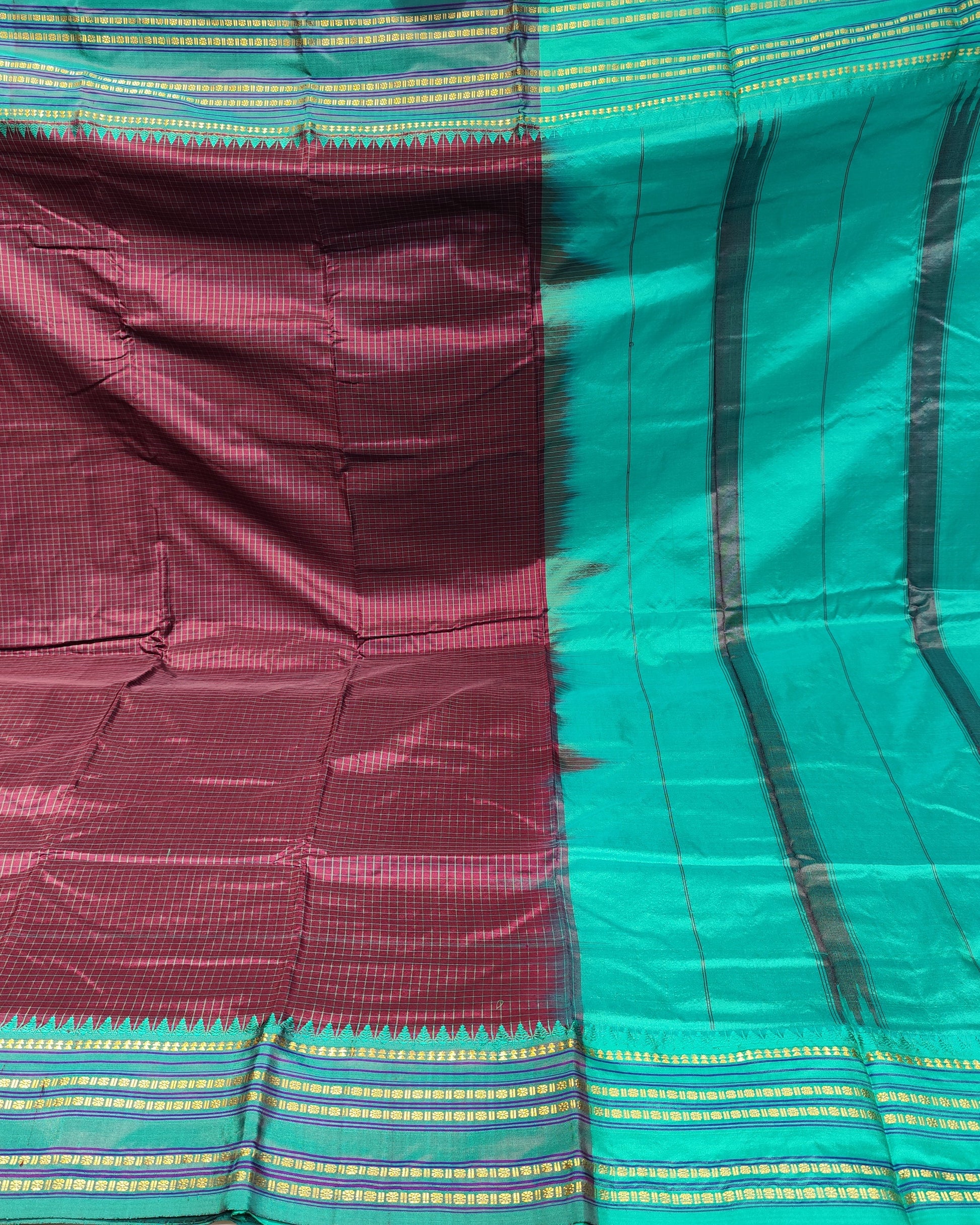 A folded and draped silk saree with a deep maroon body and a bright teal-green border, featuring black vertical stripes and gold and green woven stripes along the pallu.
